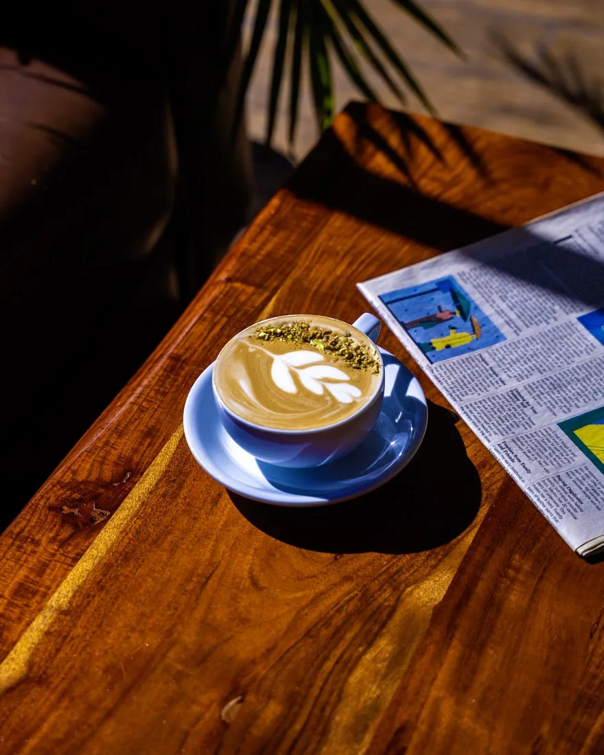 Latte in a blue cup on a sunlit café table, photographed by NG Studios